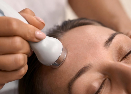 Beautician guiding a handheld device across a relaxed client's forehead – skin analysis at AFACIAL in Vienna